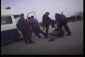 Policija u civilu udara jednog Falun Gong praktikanta na Trgu Tiananmen u Pekingu, dok je drugi praktikant silom ukrcan u policijski kombi. - Scena iz dokumentarnog filma CBC-a 